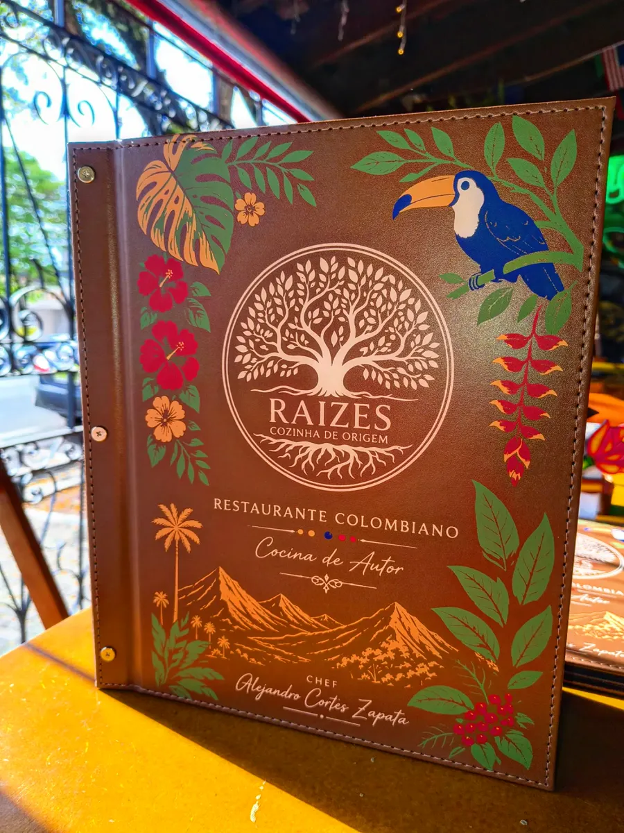 Capa de couro do cardápio com a árvore da Raízes, tucano azul, hibiscos e montanhas