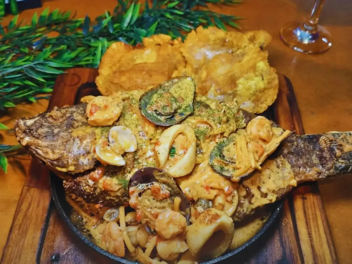 Tilápia inteira frita coberta com molho cremoso de camarão, lula e mexilhão, com patacones ao lado
